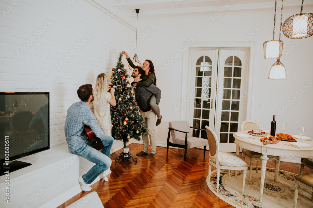 Fototapeta premium Young people decorate fir-tree for holidays of Christmas and New Year at home