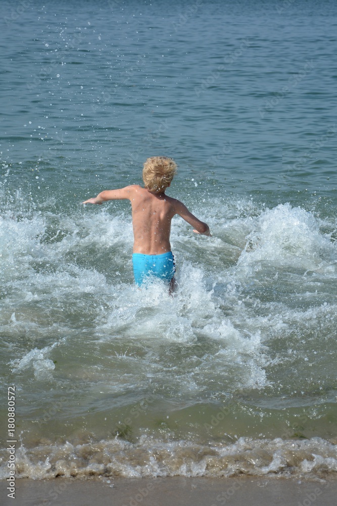 Kleiner Junge rennt in eine Welle am Meer