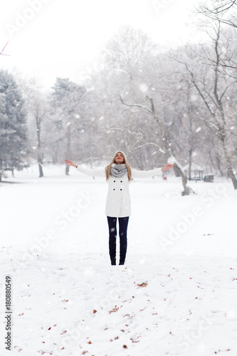 Winter portrait of beautiful blonde young woman in park with open arms.