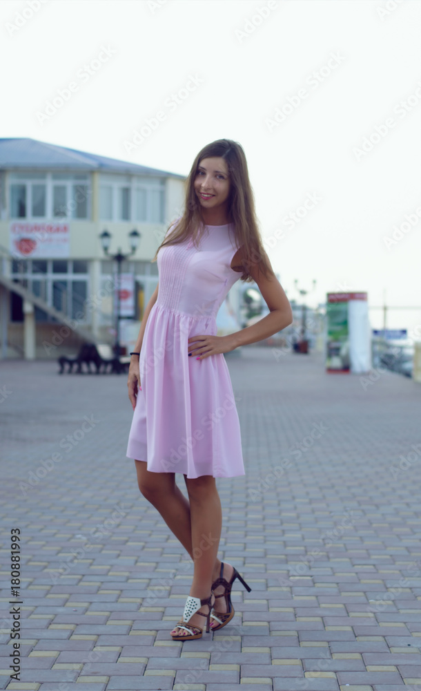 Young caucasian smiling girl with long hair standing and posing on tiled road alley on the seafront.