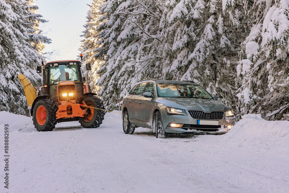 The tractor pulls a snowy car in the snow in winter landscape in Sumava. South Czech.