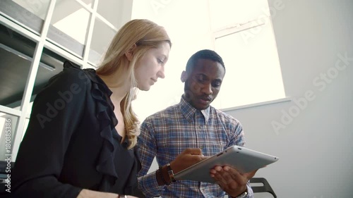 Woman and afroamerican man talking, using tablet in modern office