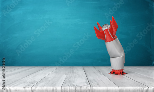 3d rendering of a red and silver realistic model of a retro rocket stands crashed into a wooden desk on a blue background.