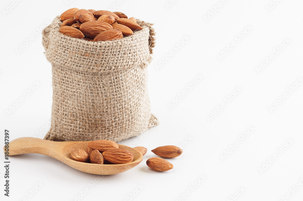Almonds in sack and wooden spoon isolated on over white background
