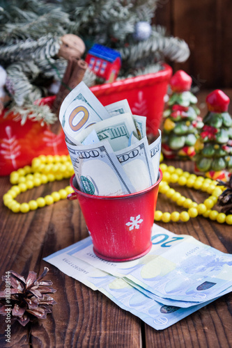 Twisted bills of dollars and euros in red christmas bucket, euro and pink macaroons. New year`s gifts