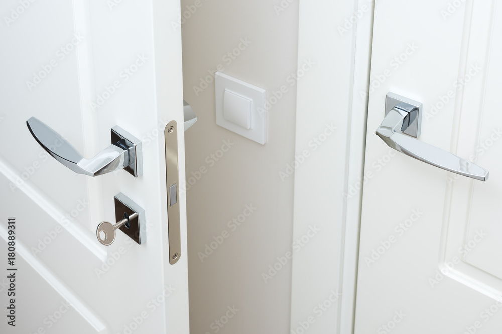 Modern chrome door handle and lock with key. White interior door closeup