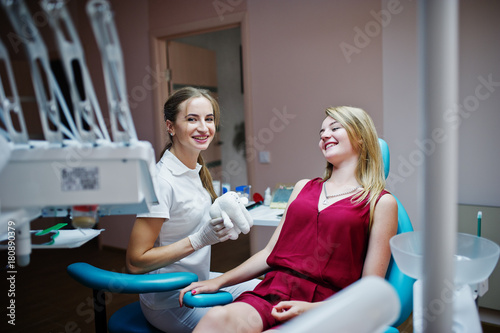 Gorgeous young orthodontist posing with big tooth model next to her pretty patient.