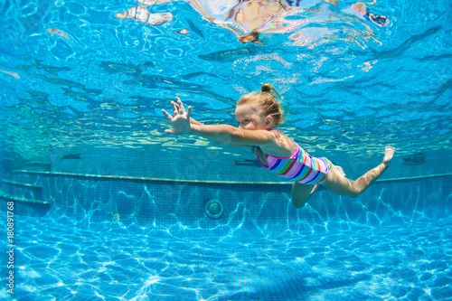 Funny portrait of child learn swimming, diving in blue pool with fun - jumping deep down underwater with splashes. Healthy family lifestyle, kids water sports activity, swimming lesson with parents.
