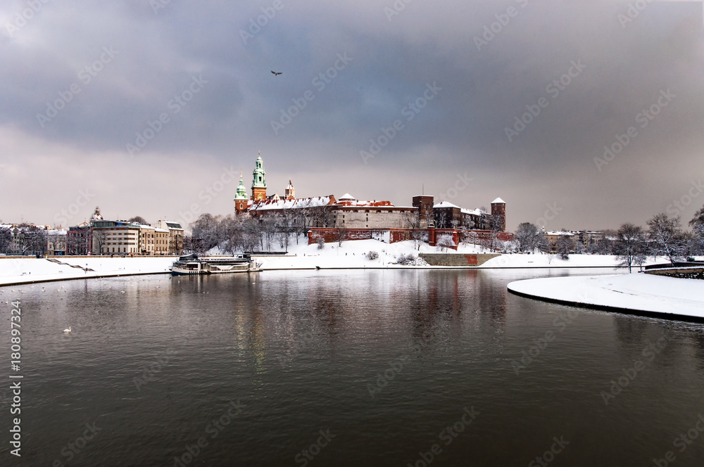 Historic royal Wawel Castle and Cathedral in Cracow, Poland, with Vistula River on a cloudy day in winter with cathedral towers in last sunlight beams before the rain