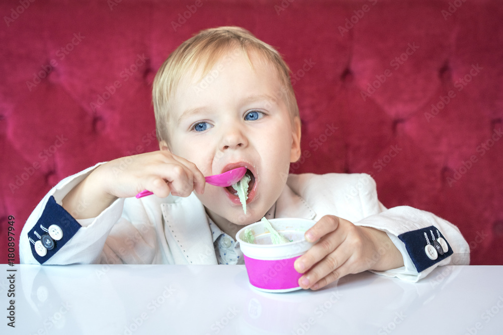 beautiful caucasian boy in a businessman's business suit in a hurry eating ice cream at restaurant during lunch. beautiful caucasian boy in a businessman's business suit in a hurry eating ice cream at restaurant during lunch.