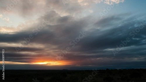 A tilt down timelapse at sunset with dramatic and dark clouds as the orange sky fades to dark blue over a wide bushveld landscape. 