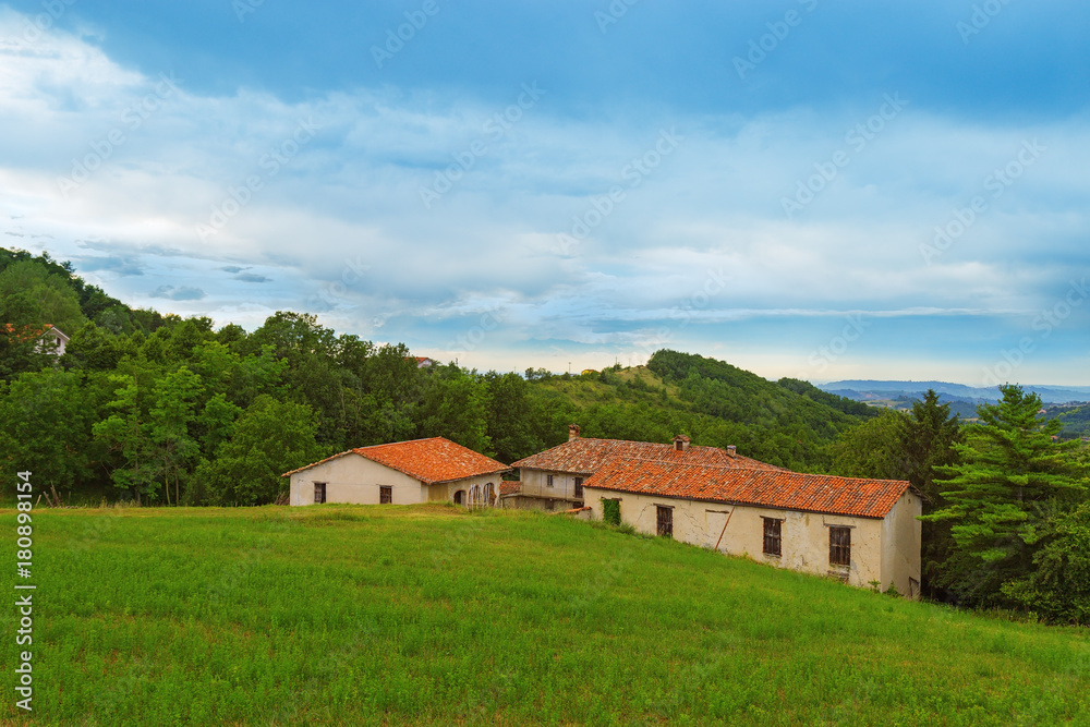 Old decaying abandoned house in the countryside of Italy is standing on green grass among the trees.