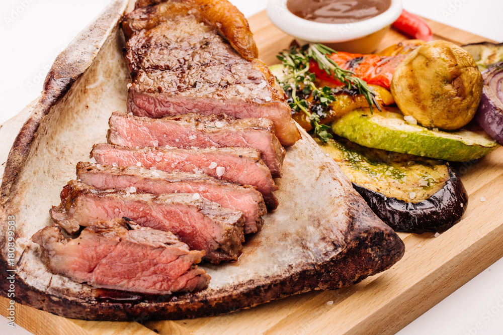 grilled beef steak on the bone with seasonings, fresh rosemary and grilled vegetables on a white background grilled beef steak on the bone with seasonings, fresh rosemary and grilled vegetables on a white background
