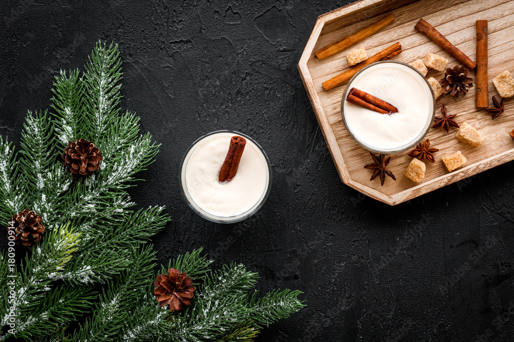 Homemade classic eggnog with cinamon and badian on wooden tray near spruce branch, pinecones on black background top view Homemade classic eggnog with cinamon and badian on wooden tray near spruce branch, pinecones on black background top view