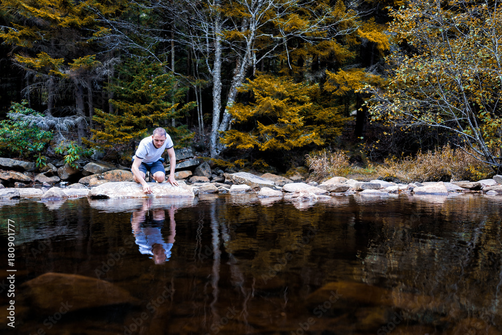 Young man looking into reflection of dark water touching with hand on peaceful, calm Red Creek river in Dolly Sods, West Virginia Young man looking into reflection of dark water touching with hand on peaceful, calm Red Creek river in Dolly Sods, West Virginia