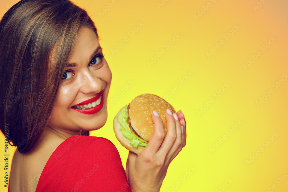 Smiling girl holding burger looks over shoulder. Smiling girl holding burger looks over shoulder.