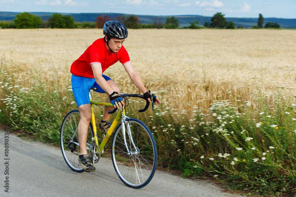 A cyclist rides on a road bicycle along field.