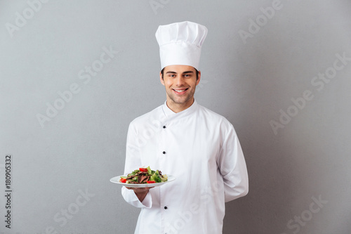 Happy young cook in uniform holding salad. photo
