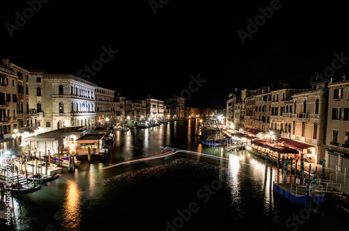 A late night long exposure view of the popular Grand Canal in Venice, taken from the top of the Ponte Rialto Bridge, with a light trail set provided by a boat manoeuvring in the moorings.