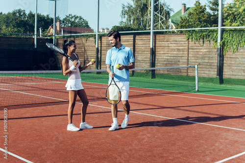 Enjoying spending time together. Full length of beautiful young couple looking at each other on the tennis court with smile.  © MARIIA