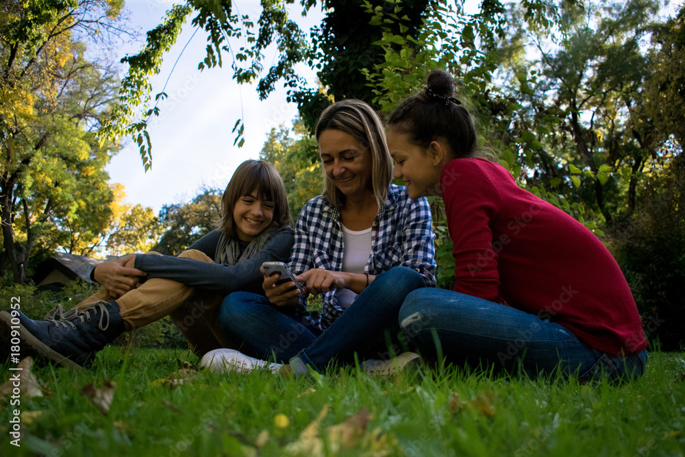 Happy family relaxing in grass at the park and using cell phone. Happy family relaxing in grass at the park and using cell phone.