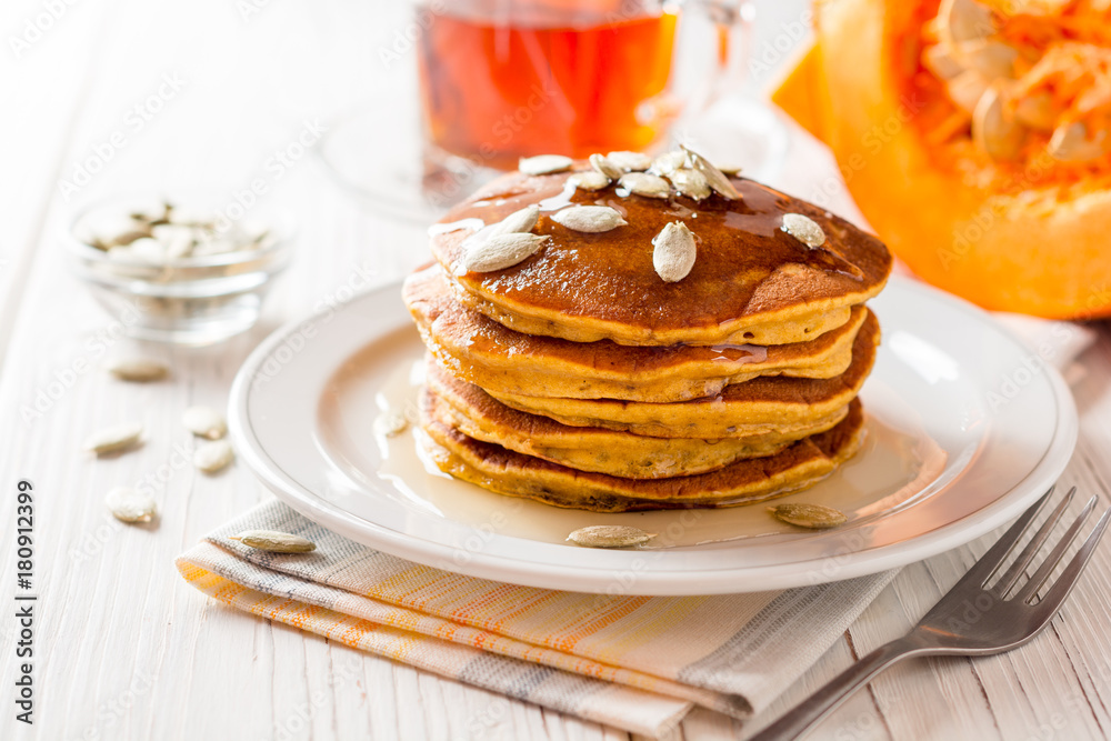 Pumpkin pancakes with honey and pumpkin seeds in plate on white wooden background.