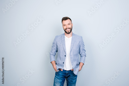Success concept. Stylish young smiling bearded brunet is standing on pure gray background. He looks so classy! in smart casual outfit, his hands are in pockets © deagreez