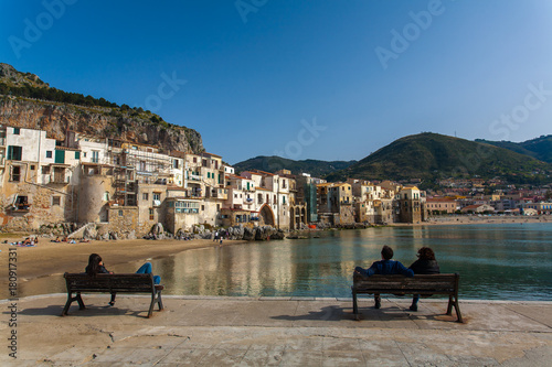 Sicily, Cefalu, Palermo. A special view of the old town of fishermen, facing directly the beach, observed from the dock by these people sitting on benches.