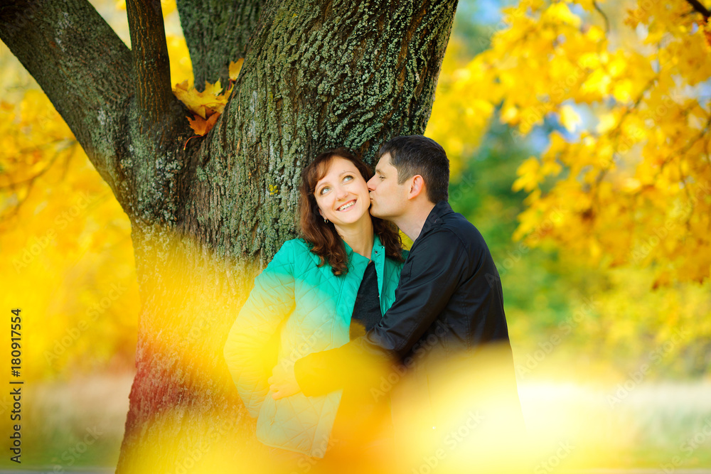 happy couple hugging and standing in a beautiful park under a big tree, bright saturated autumn foliage.