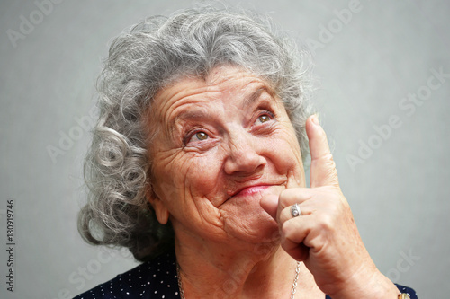 Thoughtful elderly woman points a finger up