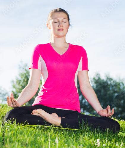 Adult woman in pink T-shirt is sitting and meditating © JackF