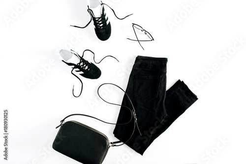Fashion woman clothes look on white background. Flat lay, top view. Sneakers, clutch, jeans and glasses.