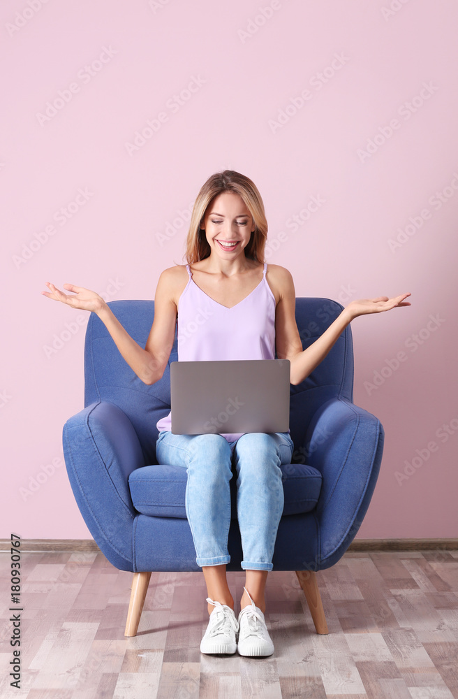 Young woman with laptop in armchair against pink wall Young woman with laptop in armchair against pink wall