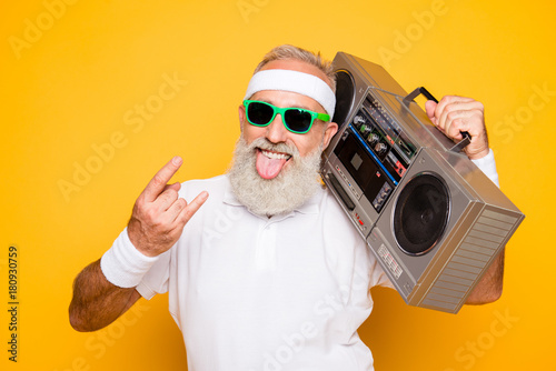 Cheerful excited aged funny active sexy athlete cool pensioner grandpa in eyewear with bass clipping ghetto blaster recorder. Old school, swag, sticking tongue, fooling, gym, workout, technology photo