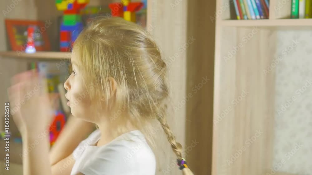 Funny little girl in singing standing in children's room, moving and laughing