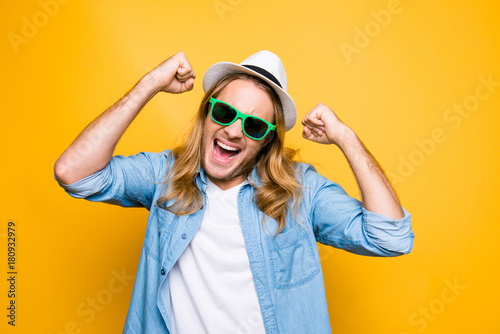 Closeup portrait of bitter displeased upset angry hipster man screaming with open mouth and clenching his fists standing over yellow background. Negative human emotion facial expression feeling