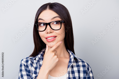 Attractive pretty girl in casual clothing and spectacles is thinking about new steps in career ladder, she is isolated on grey background