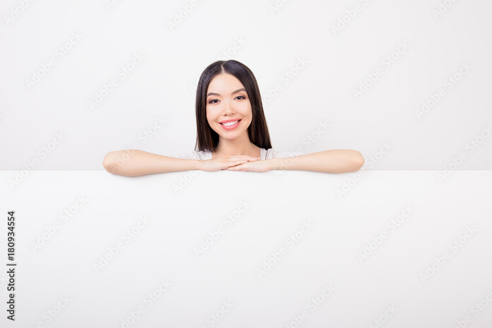 Smiling young lady in white tshirt with beaming smile is leaning on the top of an empty clean banner, she is isolated on grey background Smiling young lady in white tshirt with beaming smile is leaning on the top of an empty clean banner, she is isolated on grey background
