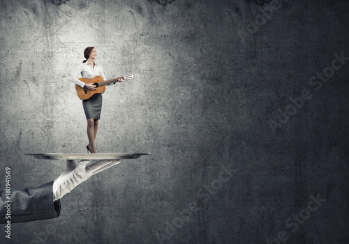 Attractive businesswoman on metal tray playing acoustic guitar against concrete wall background