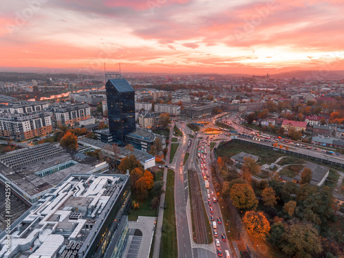 Modern architecture office building, Transportation, rush hour traffic, cars on highway interchange in city center. Sunset time, orange and gold light skyline. Drone aerial view of Krakow, Poland. 