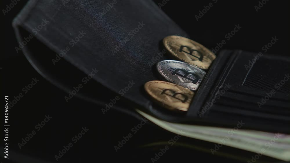 Bitcoin and paper currency are in a black wallet. Black background. Close-up Bitcoin and paper currency are in a black wallet. Black background. Close-up