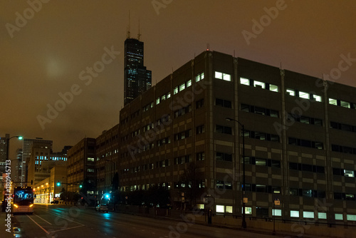 A foggy Chicago night by the Sears Willis Tower with a bus and urban parking garage.