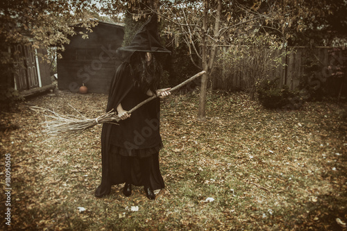 Canvastavla Creepy witch holding a broom in a country backyard during autumn.