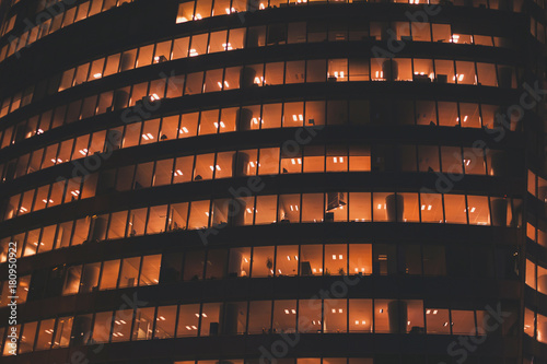 yellow light in windows of office building by night, business tower exterior
