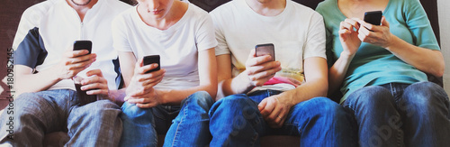 group of teenagers sitting together but all looking at their smart phones, young people with mobiles