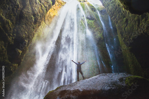 travel to Iceland, person with raised hands standing in waterfall Gljufrabui, inspired happy traveler enjoying nature, adventure concept. photo