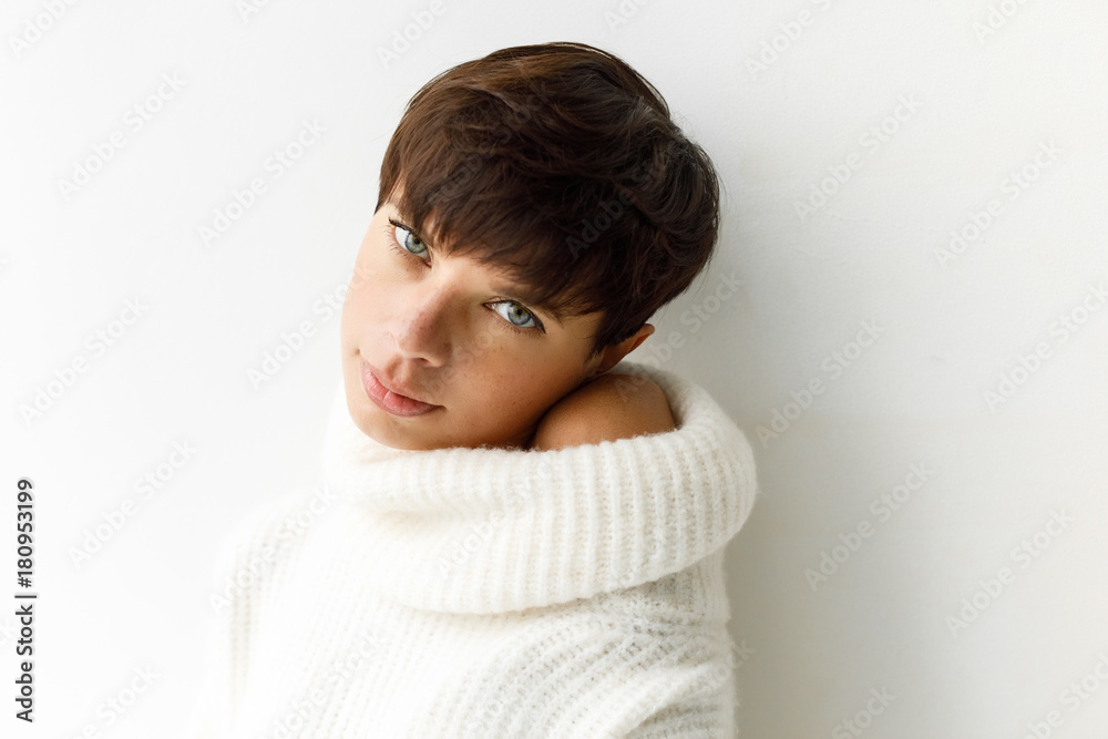 Portrait of young charming woman with short haircut posing in white sweater looking at camera. Portrait of young charming woman with short haircut posing in white sweater looking at camera.