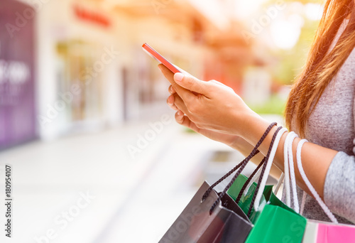 Woman holding shopping bags doing online shopping on her mobile phone in the supermarket. Black Friday sale concpt.