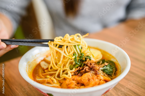Hand with Chinese chopsticks eating noodle, a famous Malaysia prawn noodle cerry soup. photo