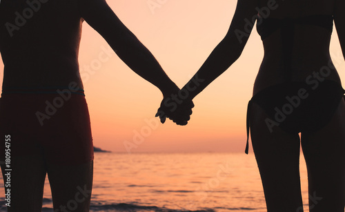 romantic travel, couple on the beach, silhouette of man and woman holding hands at sunset